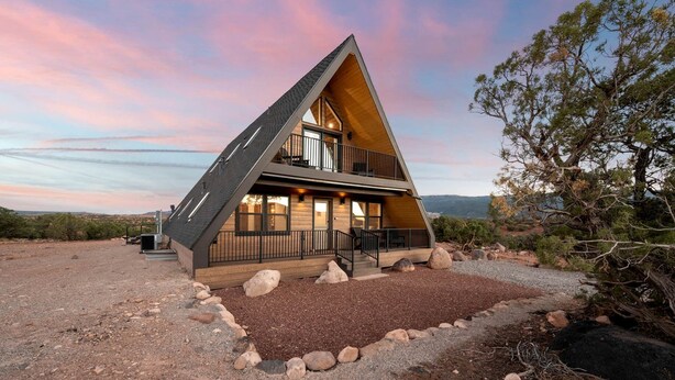 Una moderna casa a forma di A con un balcone, immersa in un paesaggio desertico con vista libera sulle colline circostanti.
