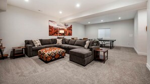 A living room with a sectional sofa, ottoman, and a painting on the wall. - Experience Pure Glamping on this A-frame Placed in the Middle of the Desert in Wayne County, Utah (Wayne County)