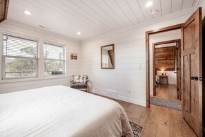 A bedroom with a bed, a chair, a mirror, and a wooden door leading to a bathroom. - Experience Pure Glamping on this A-frame Placed in the Middle of the Desert in Wayne County, Utah (Wayne County)