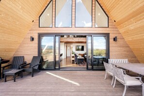 A modern loft-style building with a wooden interior and a glass door entrance leading to a dining area with outdoor seating. - Experience Pure Glamping on this A-frame Placed in the Middle of the Desert in Wayne County, Utah (Wayne County)