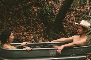 A man and a woman in a bathtub outdoors surrounded by trees. - Peaceful Cabin Stay with Fire Pit, Sauna & Mountain Adventure in Zirconia, North Carolina (Zirconia)