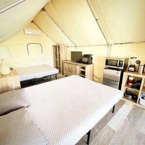 Eine Zelthotelunterkunft mit Bett, Fernseher, Mikrowelle und einer kleinen Küchenzeile.