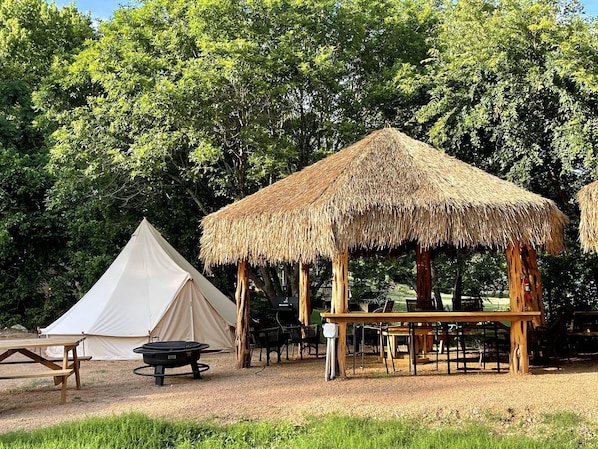 Ein Campingplatz mit Zelt, einer Holzhütte mit einem Reetdach und einem Picknicktisch.