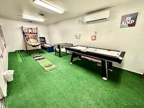 Una habitación con mesa de fútbol de mesa, mesa de ping pong y aro de baloncesto.