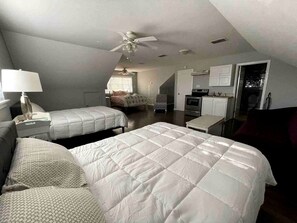 Une chambre avec deux lits, un ventilateur de plafond, un bureau et un coin cuisine.