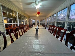 Un espace repas abrité, avec une longue table, des chaises en bois et de grandes fenêtres.