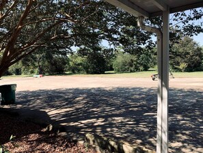 A covered outdoor area with a concrete floor, a tree, and a green trash bin. - Elevate Your Reunion: Saucier, MS Rental Offering Unrivaled Luxury and All Desired Amenities (Saucier)