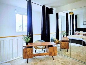 A modern bedroom with a large mirror, a wooden desk, a bed, and a view of the city. - Sea View and Cozy Apartment (Sunderland)