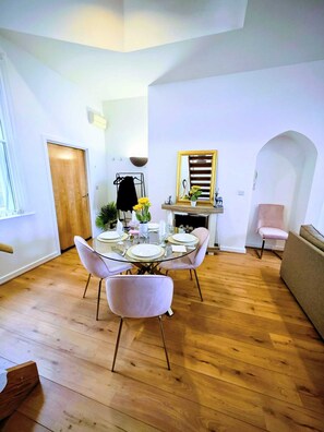 A dining area with a round glass table, pink chairs, and a wooden floor. - Sea View and Cozy Apartment (Sunderland)