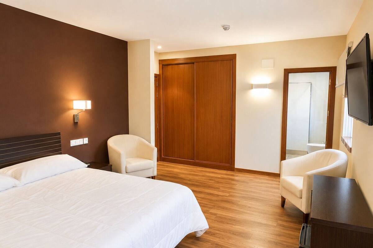 Habitación de hotel con cama, dos sillas, armario de madera, televisor y espejo.