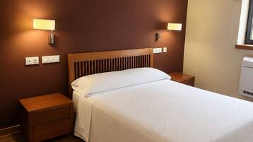 A neatly arranged bedroom with a wooden headboard, two bedside tables, a bed with a white bedspread, and wall-mounted lamps.