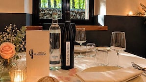 A dining table set with a bottle of water, a bottle of wine, and empty wine glasses, a bread roll, and a plate with rose petals. - Hospederia La Serrana (Piornal)
