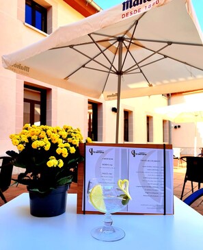 A table with a menu, a potted plant with yellow flowers, and an umbrella. - Hospederia La Serrana (Piornal)