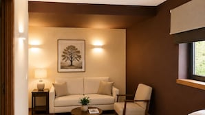 A hotel room with a bed, a sofa, a chair, a small table with a plant, a lamp, and a framed picture on the wall. - Hospederia La Serrana (Piornal)