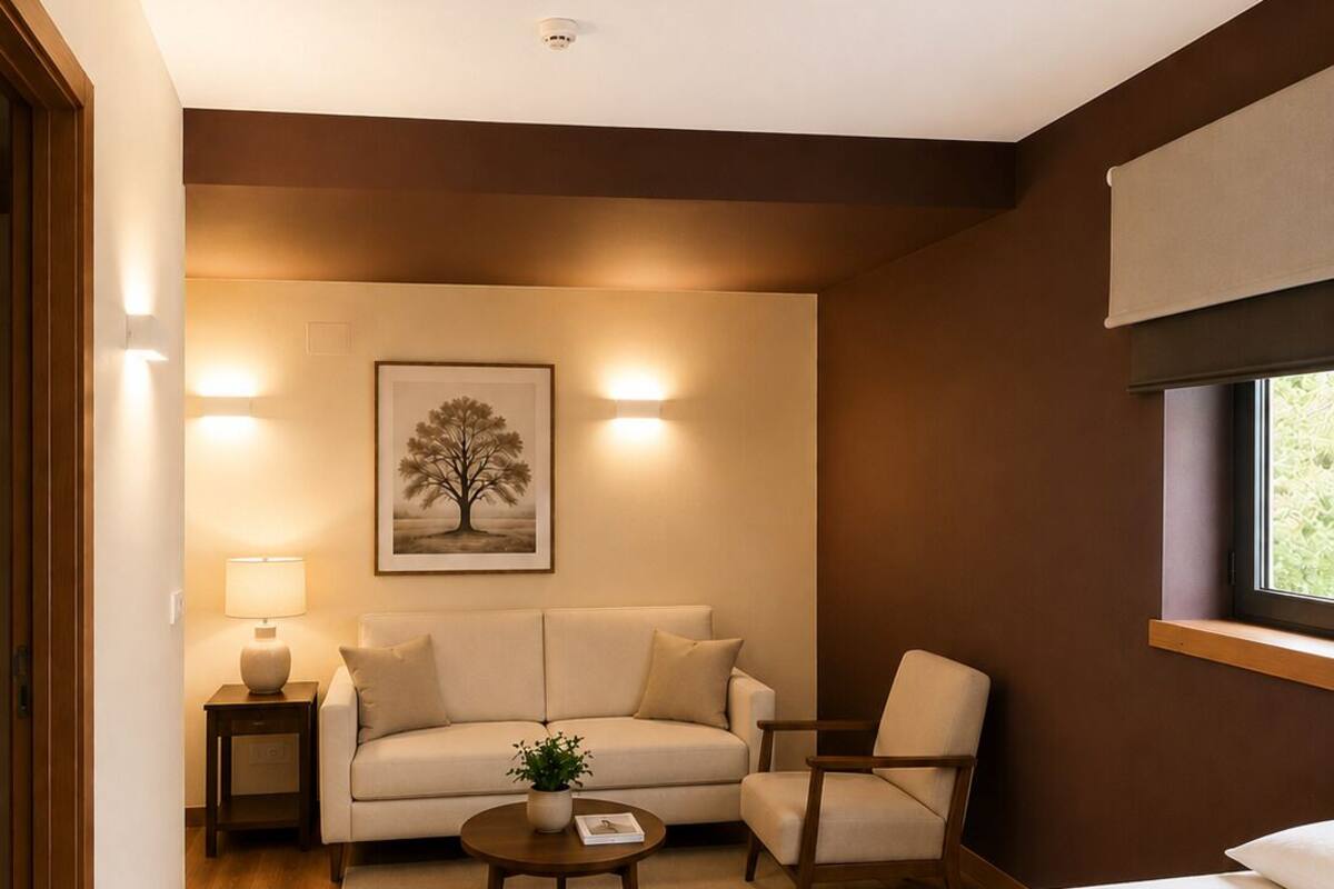 Una habitación de hotel con una cama, un sofá, una silla, una mesita con una planta, una lámpara y un cuadro en la pared.