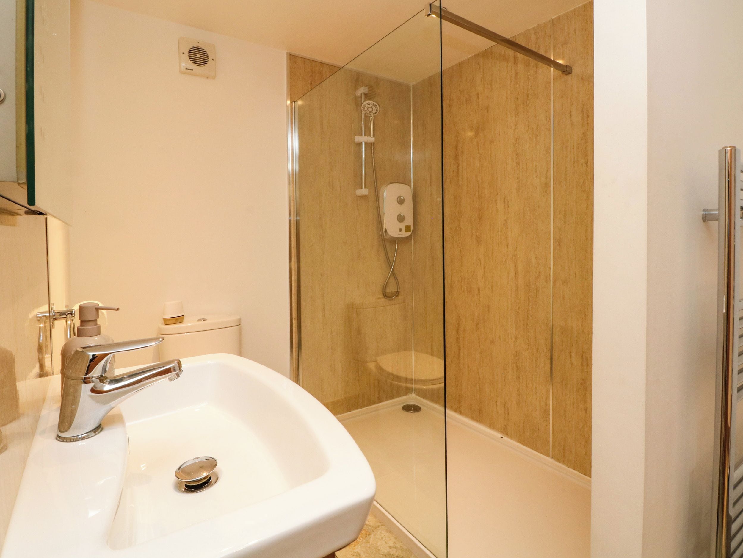 Un baño moderno con ducha envuelta en vidrio, un lavabo blanco y un inodoro.
