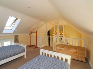 A bedroom with two beds, a wooden dresser, a white railing, and a skylight. - Plas Tirion Cottage (Holywell)
