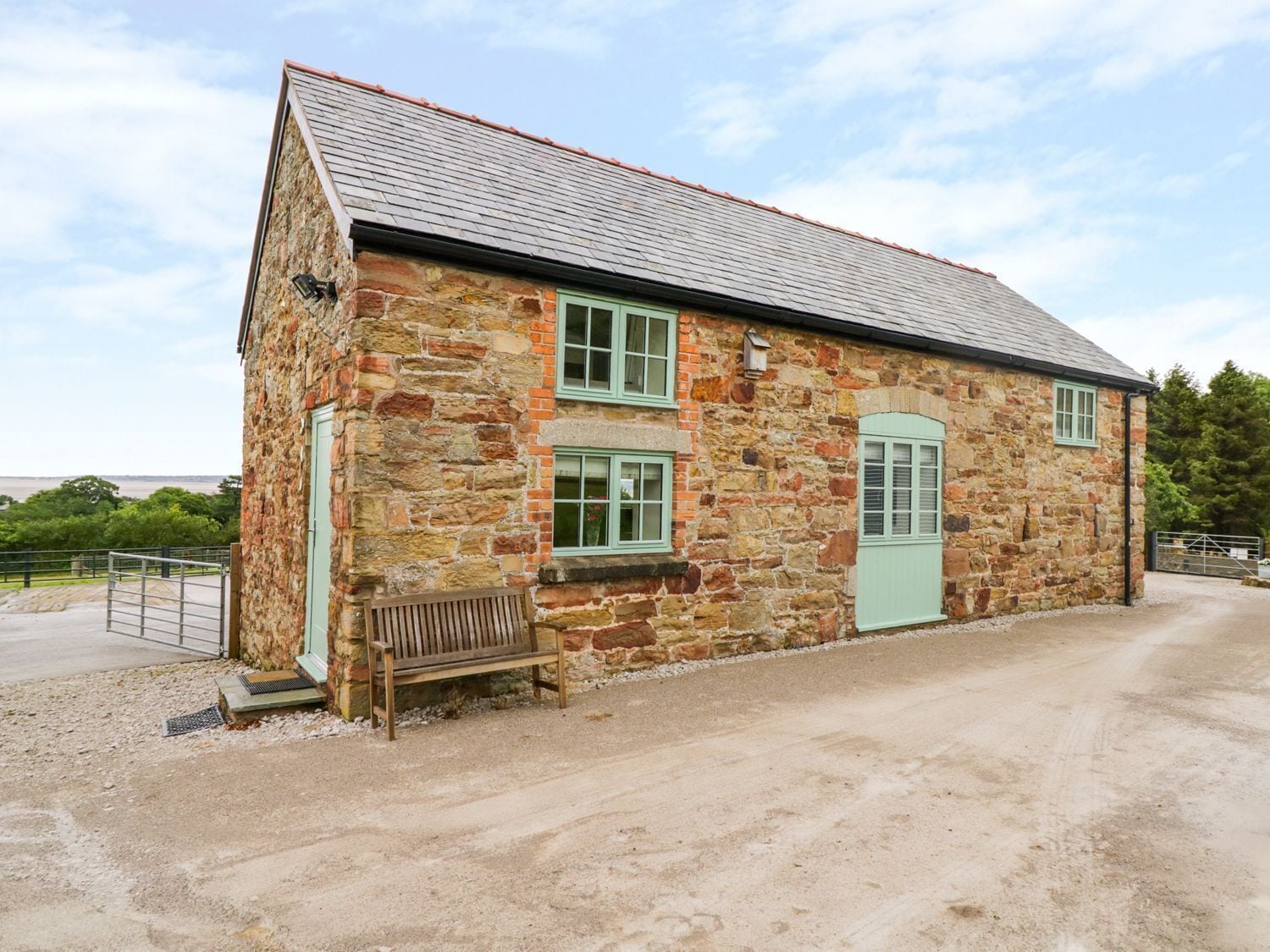 A stone building with a green door and windows, a bench outside, and a gravel driveway.