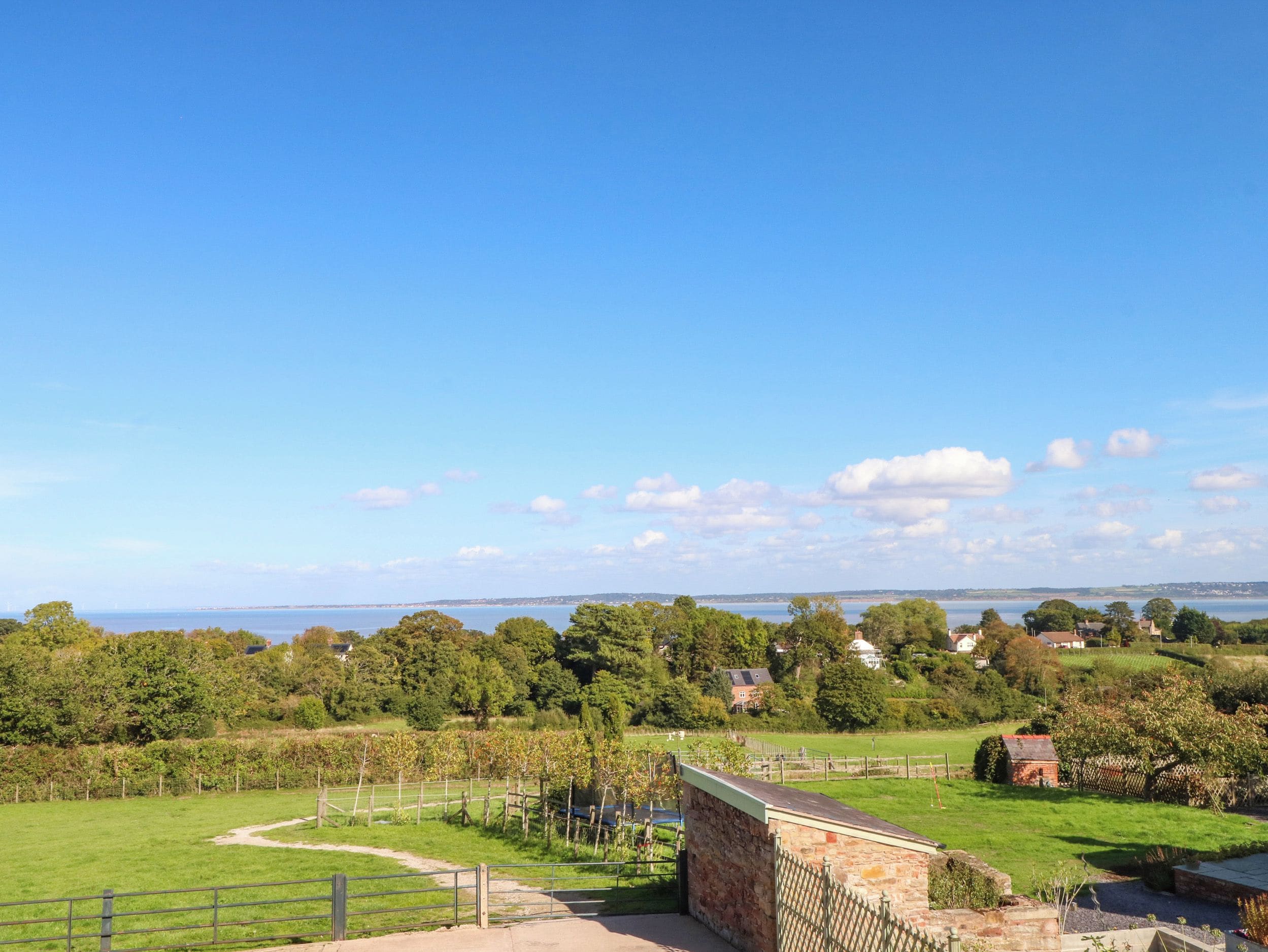 A rural landscape with a clear sky, a fenced field, and a stone building with a sloped roof.