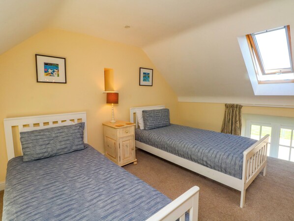 A bedroom with two single beds, a nightstand, a lamp, and a skylight.
