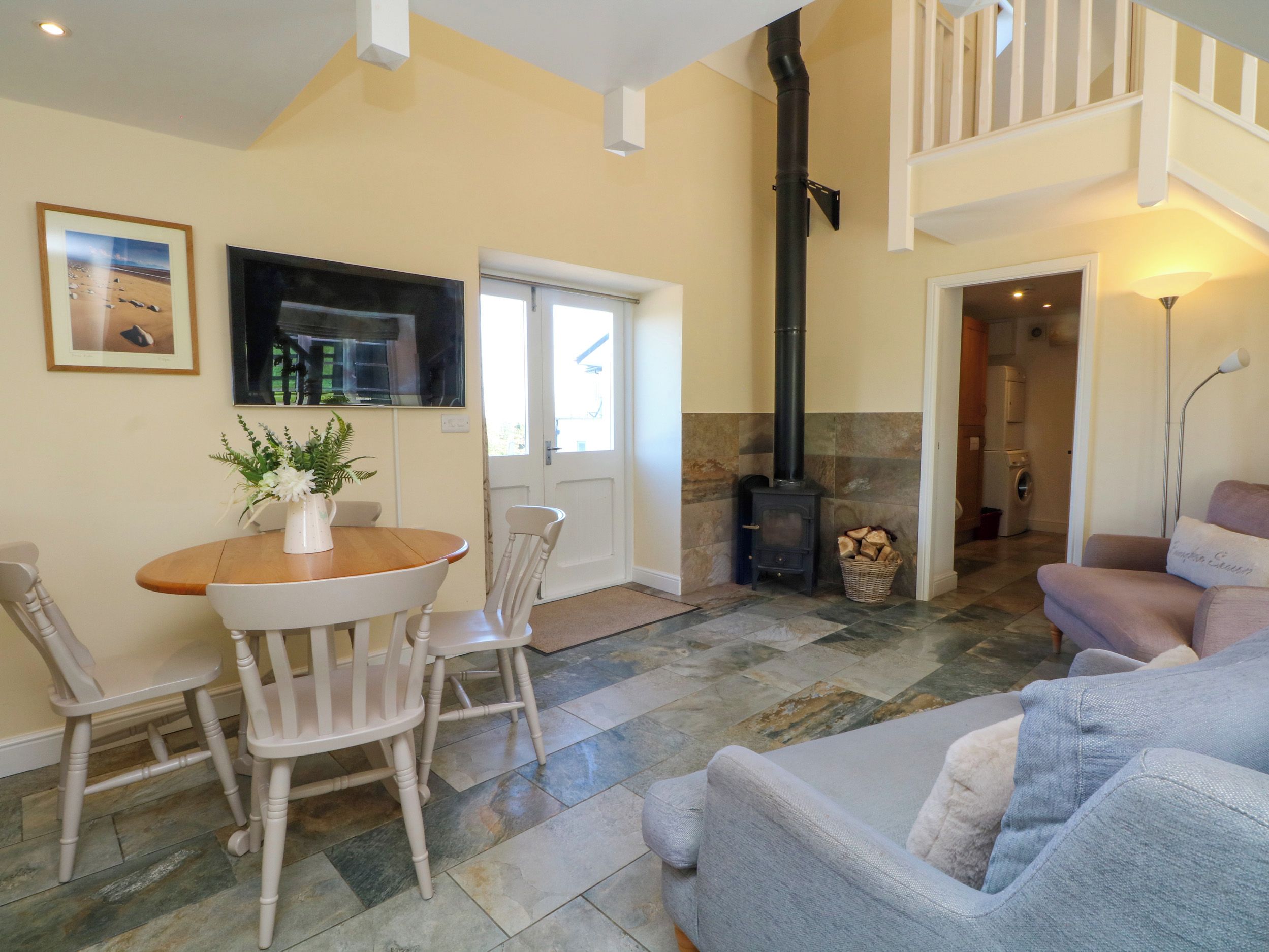 Una sala de estar con chimenea, un comedor con sillas y una mesa, y una escalera que lleva a un nivel superior.