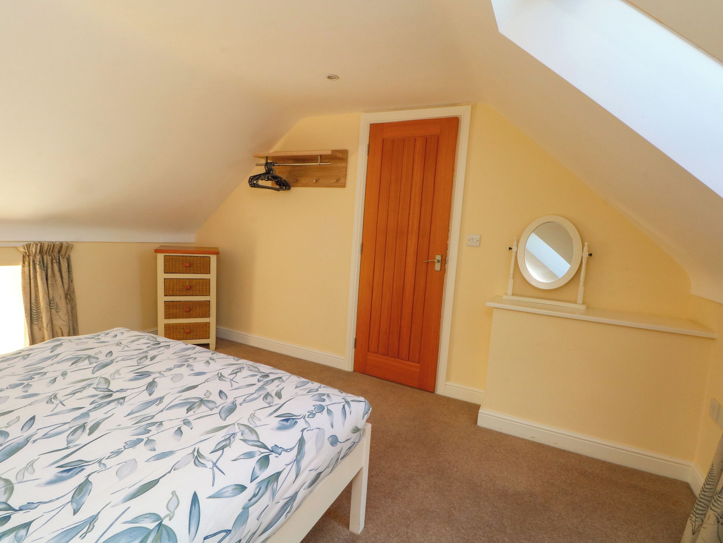 A bedroom with a bed, a wooden door, a shelf with a mirror, and a window with curtains.