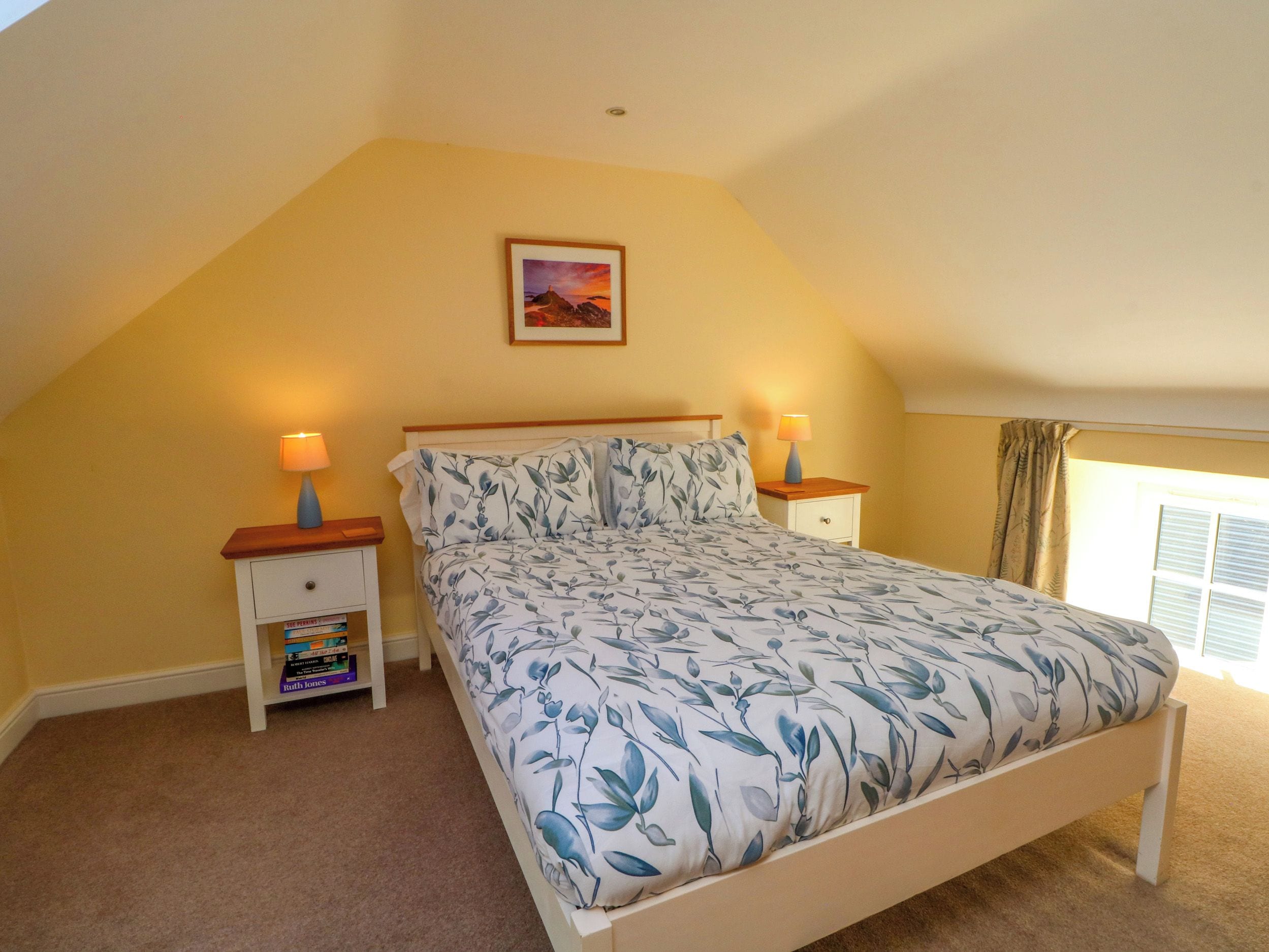 A bedroom with a bed, two bedside tables, a nightstand, a window with curtains, and a painting on the wall.