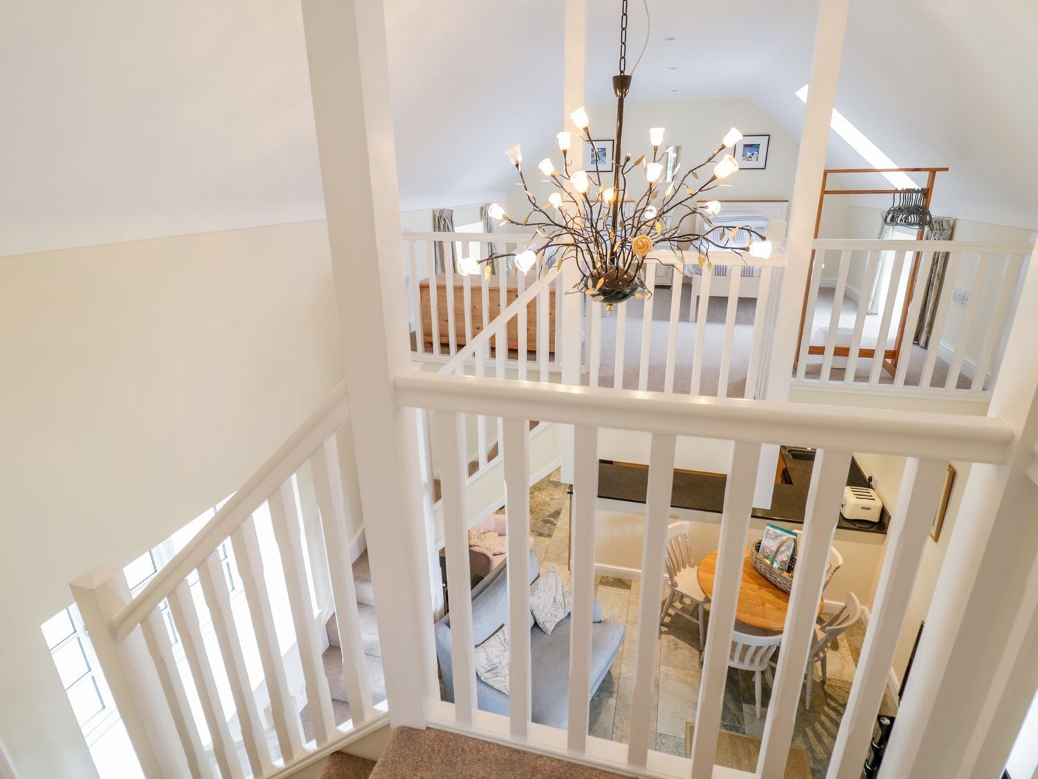 A high-ceilinged room with a chandelier, white railings, and a dining area with a table and chairs.
