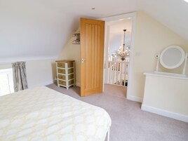 Un dormitorio con una cama, una puerta de madera, un aparador blanco y un pequeño mueble de mimbre.