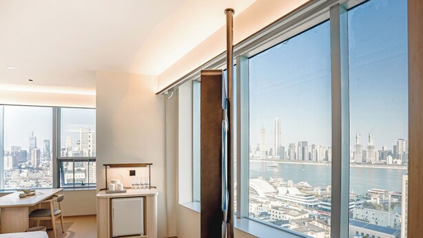 A hotel room with a large window, a desk with a chair, a bed, and a minibar. - JI Wuhan Jianghan Road Pedestrian Street (Wuhan)