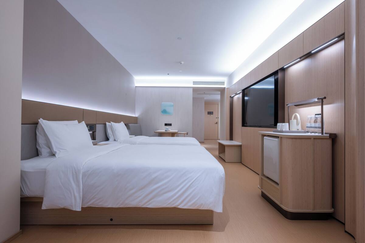 Habitación de hotel moderna con una cama grande, televisión, una kitchenette pequeña y un baño a la vista.