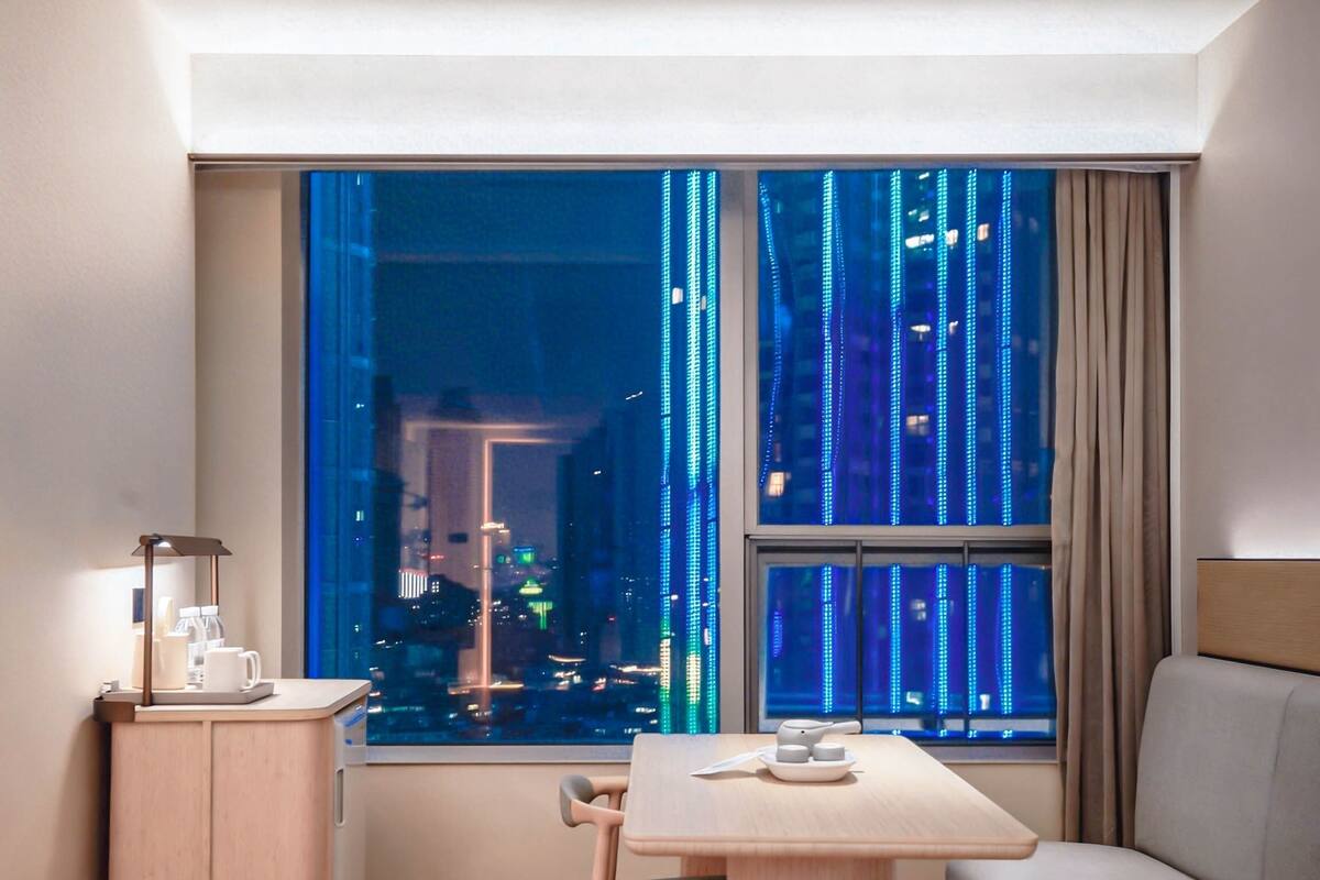 Habitación de hotel con vista a la ciudad, una mesa con una silla, una mesita de noche con una lámpara y una cama.
