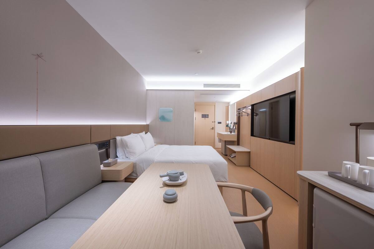 Una habitación de hotel moderna con cama, sofá, mesa de comedor, televisor y kitchenette.