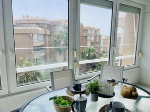 Een balkon met een tafel, een mandje groene appels, een koffiepot, een bloempot en een brood.
