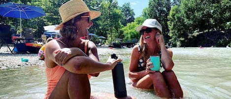 Two people in a river, one holding a camera and the other holding a mug.