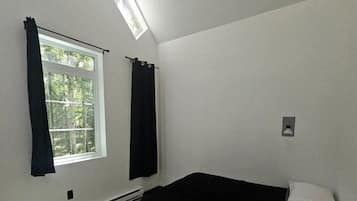 A room with a bed, a window with curtains, a skylight, and a thermostat.