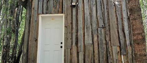 Una cabaña de madera rústica con una puerta blanca, rodeada de árboles.