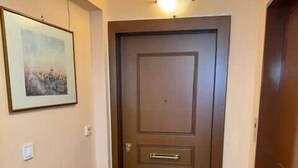 A hallway with a wooden door, a framed picture on the wall, a dark-colored desk, and a tiled floor. - Cozy & Cute Apartment in Piraeus (Pireas)