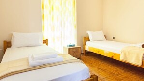 A room with two beds, a wooden floor, a nightstand, and a window with curtains. - Cozy & Cute Apartment in Piraeus (Pireas)