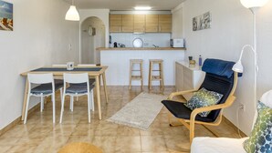 Un espace de vie compact comprenant un coin repas, une kitchenette et un coin salon avec un fauteuil et un canapé.