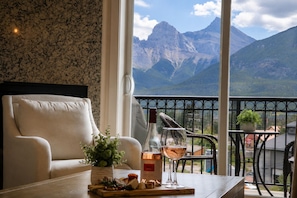 A room with a view of mountains, a sofa, a table with a bottle and glasses, and a balcony with a railing. - Penthouse with Waterpark | Sleeps 8 | Spacious | Views (Canmore)