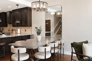A modern kitchen with dark cabinetry, a marble countertop, and a central island with bar stools. - Penthouse with Waterpark | Sleeps 8 | Spacious | Views (Canmore)