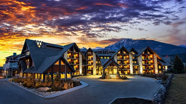 Un chalet à étages, doté d’une entrée imposante et entouré d’un paysage montagneux.
