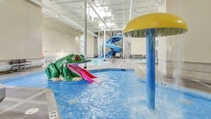 Un parc aquatique intérieur doté d’une grande sculpture de grenouille, d’un toboggan aquatique et d’un espace piscine.