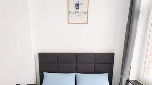 A bedroom with a bed, pillows, a nightstand, a framed sign, and a window with curtains. - 4. Bed 4D Center-Station-Airport (Charleroi)