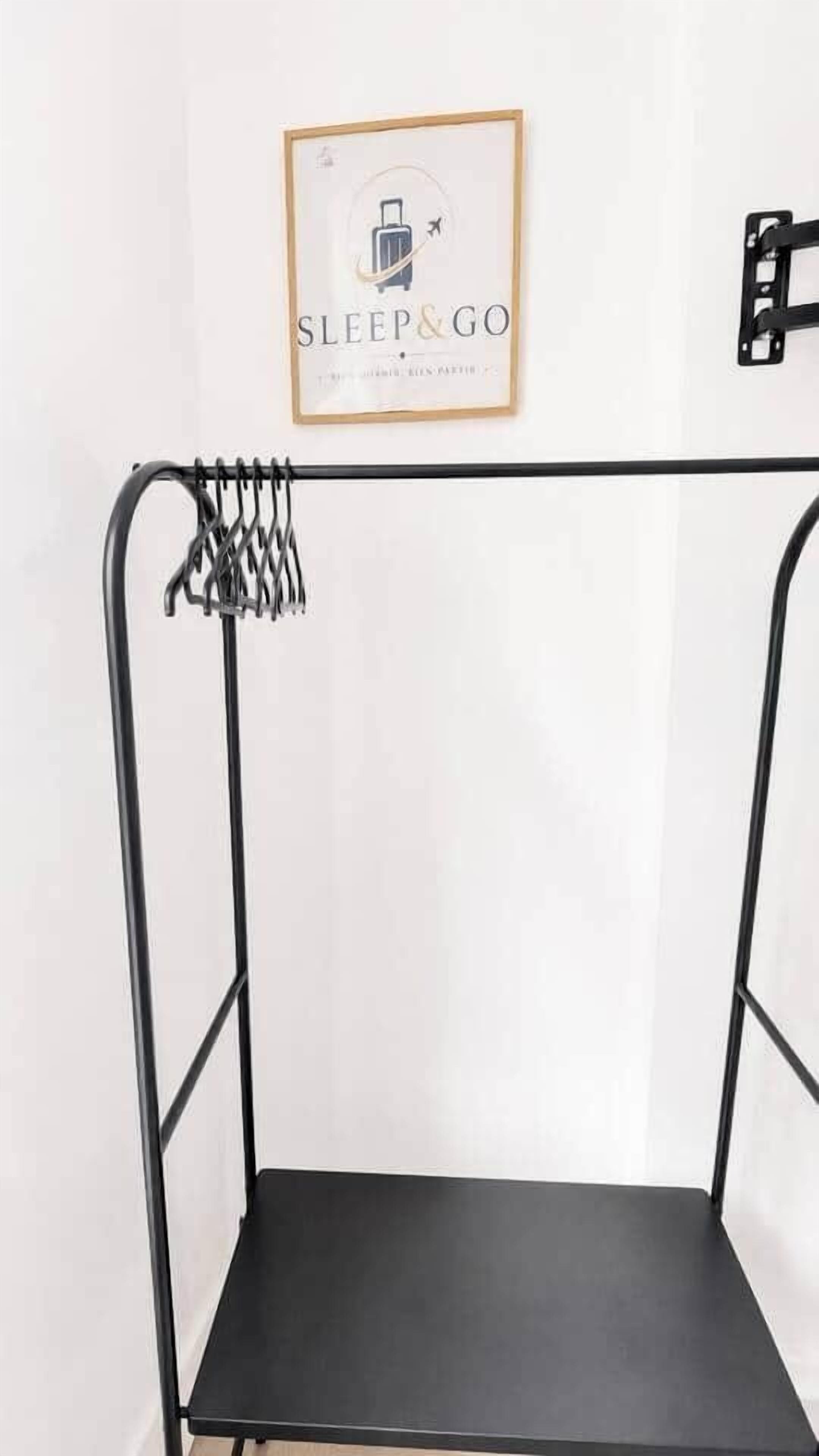 Un cadre de lit en métal avec un matelas noir, une affiche encadrée au-dessus, et un luminaire fixé au mur.