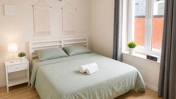 Ein Schlafzimmer mit Bett, Nachttisch, Lampe und einem Fenster mit Vorhängen.