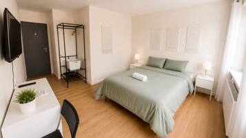 Ein Hotelzimmer mit Bett, Nachttischen, einem Schreibtisch mit Stuhl, einem Fernseher und einem Kleiderschrank.
