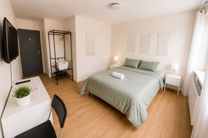 A hotel room with a bed, bedside tables, a desk with a chair, a television, and a wardrobe. - 5. Bed E5 Center-Station-Airport (Charleroi)