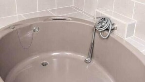 Eine Badewanne mit Duschkopf und Brause, vor einer gefliesten Wand.